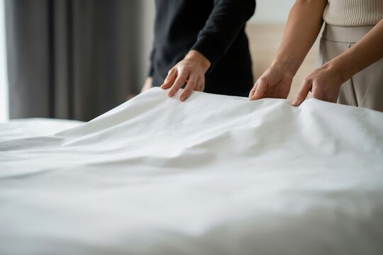 Two people making a bed with fresh white linens. Professional hotel service.