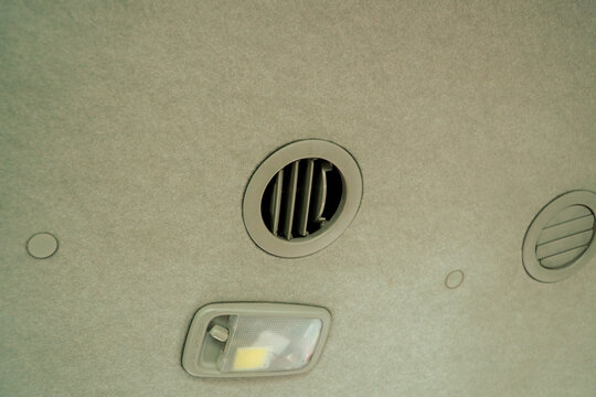 Close-up of car ceiling interior featuring air vents and overhead light switch on textured fabric surface for automotive design or vehicle comfort concept, elegantly showcasing cabin.