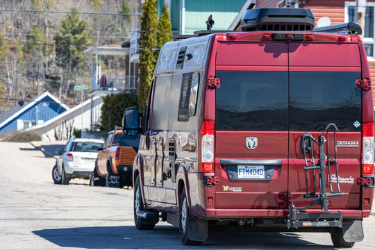 Quebec, Canada, 26 April 2026 : A red Pleasure-Way RAM Promaster camper van with a bike rack is parked on a residential street.