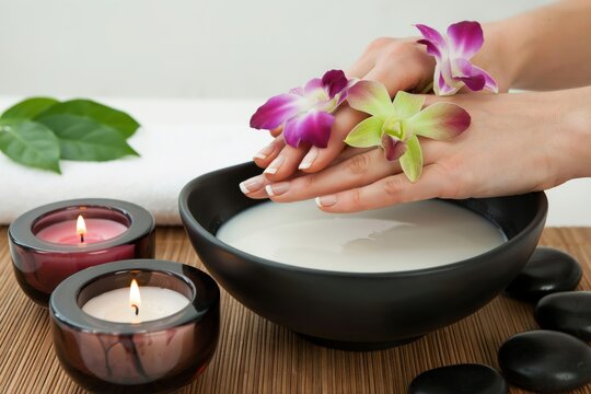 Woman hands soak in a black bowl with milk and orchids. Spa treatment concept.