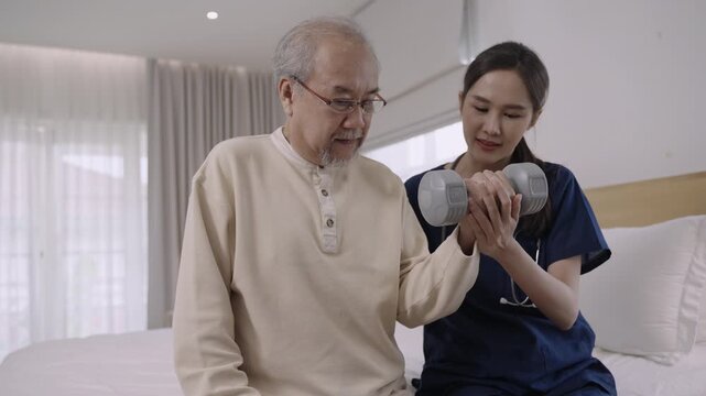 Professional Asian woman nurse physiotherapist using a dumbbell for workout exercise for physical recovery of muscles and bones of a senior man patient in hospital bed. Healthcare and medical concept.