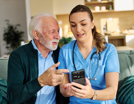 Doctor or nurse caregiver helping senior man with a mobile phone at home or nursing home