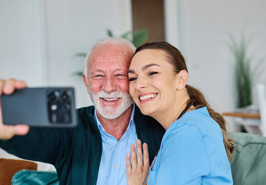 Doctor or nurse caregiver helping senior man with a mobile phone taking selfie at home or nursing home