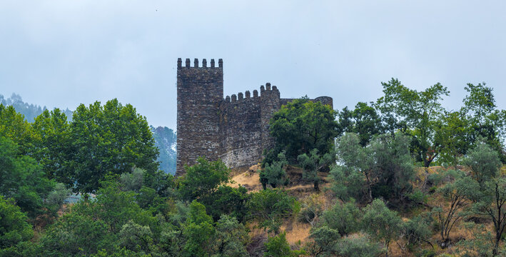 An ancient stone castle tower with battlements stands dramatically on a forested hilltop