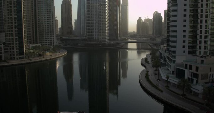 Timelapse of the Dubai Marina skyline and canal, featuring modern skyscrapers and waterfront walkways. Residential towers dominate the dense urban landscape