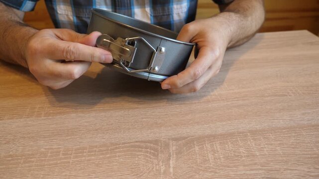 A person repeatedly opens and fastens the latch of a springform cake pan, creating a distinctive clicking sound. The video contains original sound of the latch.