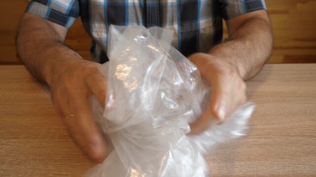 A person continuously crumples a plastic bag with hands, creating a distinctive rustling sound. The video contains original sound of plastic.