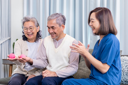 Senior couple get medical service visit from caregiver nurse while using round squishy ball for muscle strength in pension retirement center for rehabilitation and longevity post recovery process