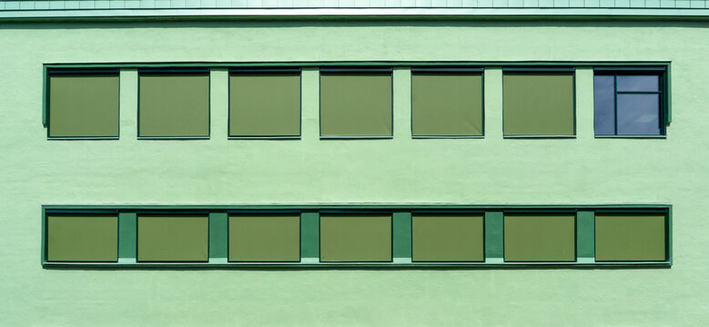 Green building facade with rows of windows and blinds