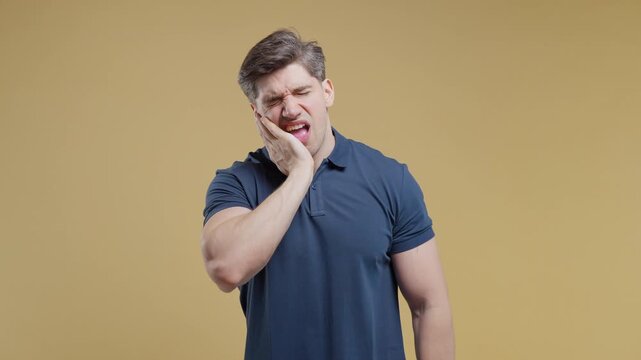 Young man touching cheek with painful expression while suffering from sudden toothache. Handsome male experiencing dental pain, oral health problems, sensitivity and discomfort. Studio portrait 