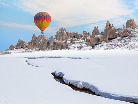 Hot air balloon flying over spectacular Cappadocia - Rock formation in Cappadocia following a heavy snow fall. Everything covered snow under sunset  sky