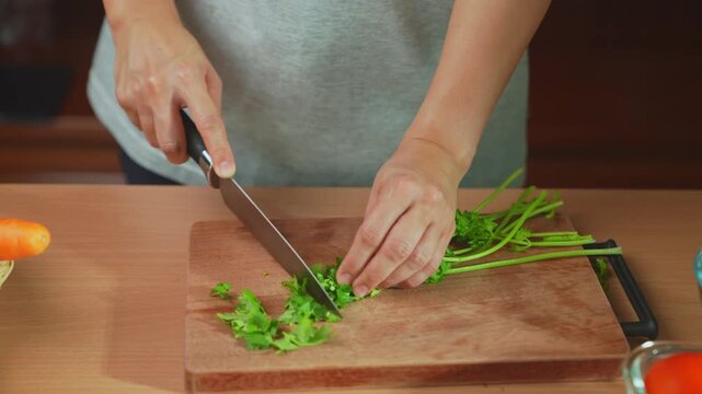 Woman hands were chopping fresh cilantro on a wooden cutting board.