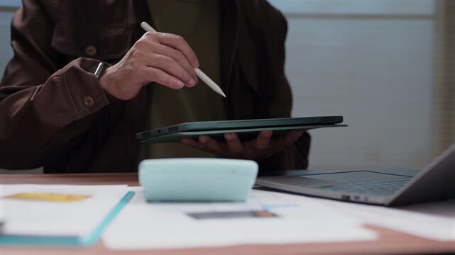 Man sits desk holding pad stylus checking finance sheet calculator laptop screen staff planning budget tasks firm career boss work team job role duty goal target scheme action.