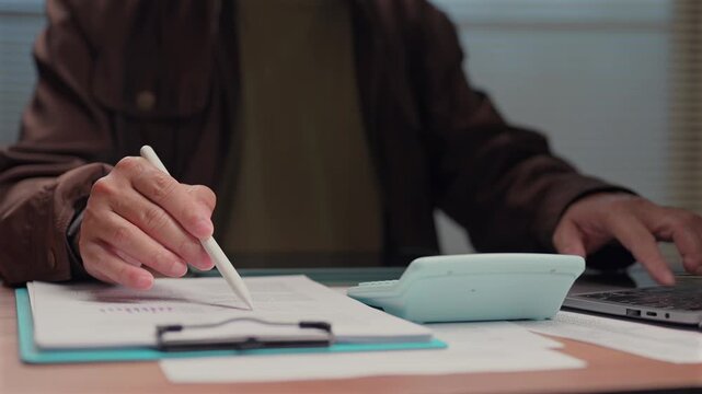 Person sits wooden desk checking financial reports calculating budget balance sheet profit margin earnings revenue investment tax cost expense audit corporate company enterprise administration.