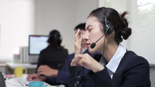 Stressed asian call center operator rubbing her eyes in the office