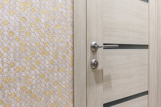 light‑beige wood‑grain interior door with horizontal dark‑grey inlays, a polished lever handle, and a matching lock. adjacent wall displays a honeycomb‑patterned wallpaper in gold and cream tones