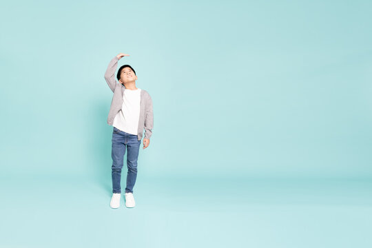 A happy Asian boy measuring his height with hand above head in studio background, representing physical growth, healthy development, child progress, and growing up with copy space