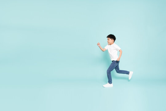 An energetic Asian boy running fast in studio against light blue background, demonstrating active lifestyle, happy childhood, dynamic play, speed, and health with ample empty copy space