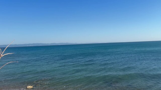 Static shot of calm blue sea waves gently washing onto the beach shore under a clear sky in Saros Gulf, Edirne, Turkey.