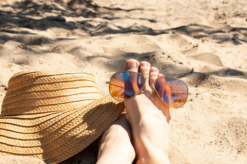 Women's legs on a sandy beach next to a straw hat and sunglasses. The theme is summer vacation, holiday, resort © Виктория Котлярчук