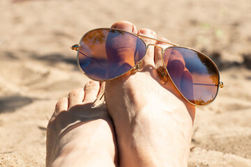 Women's legs with sunglasses on a sandy beach, themed around summer vacations, holidays, travel © Виктория Котлярчук