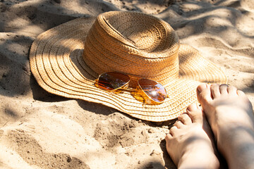 Women's legs on a sandy beach next to a straw hat and sunglasses. The theme is summer vacation, holiday, resort © Виктория Котлярчук