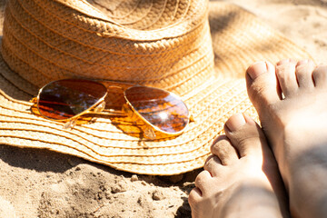 Women's legs on a sandy beach next to a straw hat and sunglasses. The theme is summer vacation, holiday, resort © Виктория Котлярчук