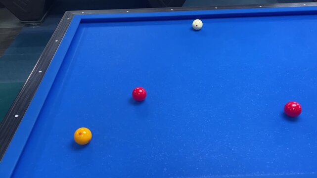 Carom billiards game with four balls on blue felt table with cue stick