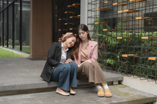 Stressed Asian businesswoman crying while colleague comforting her outside office.