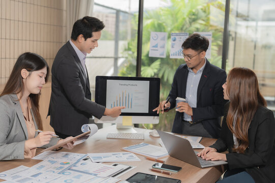 Group of serious Asian business people analyzing financial charts in office meeting.