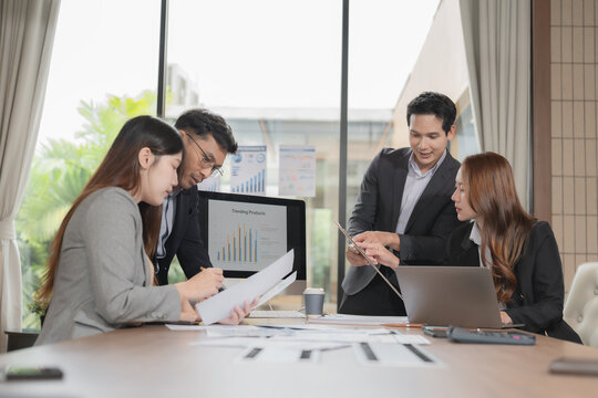 Group of serious Asian business people analyzing financial charts in office meeting.