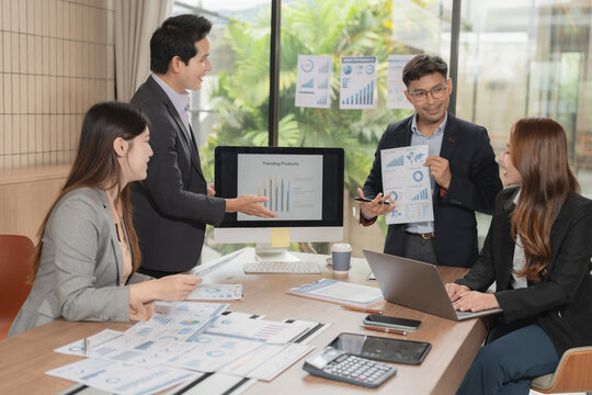 Group of serious Asian business people analyzing financial charts in office meeting.