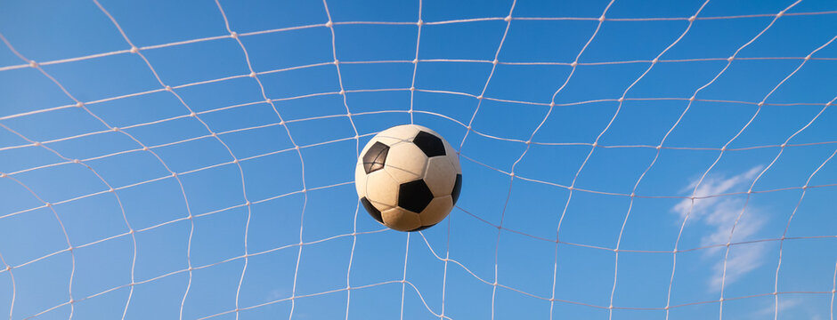 Soccer ball hitting the goal net against a clear blue sky, scoring and achieving target winning goal concept. Web banner size photo.