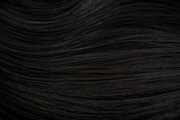 Fototapeta premium Brunette or black hair. Female long dark hair in black. Beautifully laid curls. Closeup texture in a dark key. Hairdressing, hair care and coloring. Shading gray hair. Background with copy space.