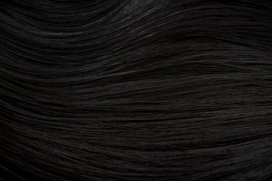 Brunette or black hair. Female long dark hair in black. Beautifully laid curls. Closeup texture in a dark key. Hairdressing, hair care and coloring. Shading gray hair. Background with copy space.