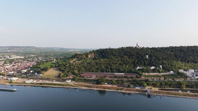 Drone aerial view of Klopp Castle hill in Bingen am Rhein, Germany, featuring the forested hillside crowned by Klopp Castle, vineyards, historic architecture and the Rhine riverside below. Scenic summ