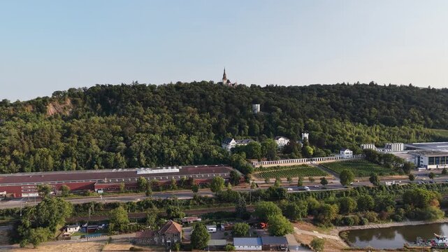 Drone aerial view of Klopp Castle hill in Bingen am Rhein, Germany, featuring the forested hillside crowned by Klopp Castle, vineyards, historic architecture and the Rhine riverside below. Scenic summ