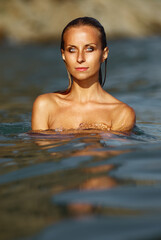Fototapeta premium A serene portrait of a young woman emerging from calm sea water at sunset, her wet skin glowing with warm golden light and reflective ripples creating a tranquil, summery mood.