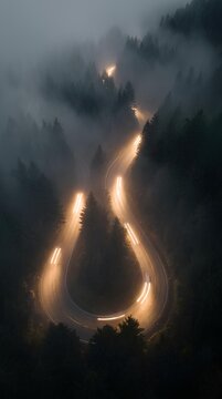Night long exposure of winding forest road with glowing car light trails through fog.