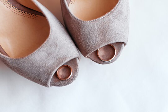 Soft suede peep-toe bridal shoes hold two gold wedding rings in minimalist close-up composition conveying romance, preparation and elegant wedding details for invitations, blogs and styled shoots.