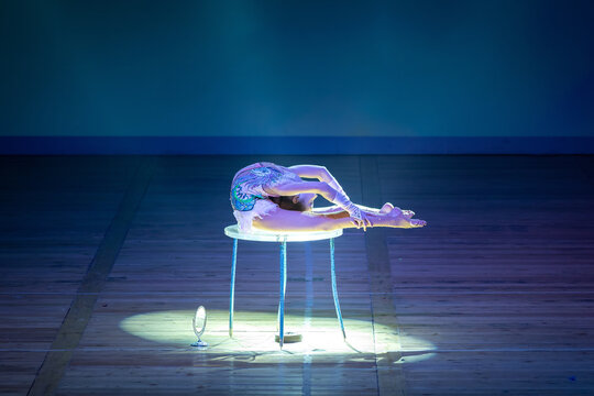 Young contortionist performing a flexible pose on a stage table. Concept: Circus art performance, extreme flexibility, and stage entertainment