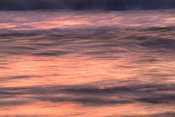 Fototapeta premium island sunset orange and purple reflected in slow moving waves on beach