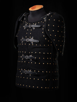 Black studded leather armor vest on mannequin against dark background, medieval costume and protective gear.