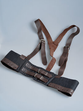 Black textile harness belt with brown leather straps and twin buckle closures displayed flat on a neutral background, showing functional fastening construction.