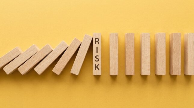 Wooden dominoes falling in a row with the word risk on one block