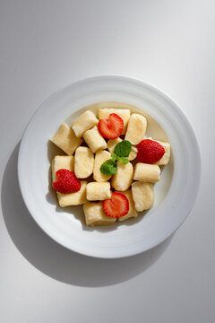 Bright, minimalist plate features soft gnocchi cubes, fresh strawberries, and a mint sprig, creating a light dessert or brunch item perfect for food photography and recipe catalogs.