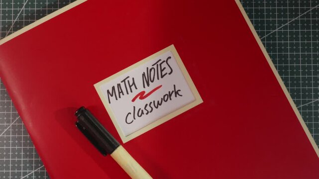 Red Math Notes Classwork workbook on wooden tabletop
