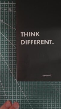 Hand adjusting Think Different notebook on green cutting mat