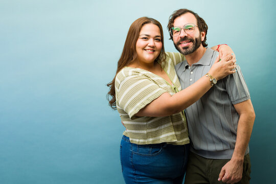 Portrait of a couple embracing, standing together and smiling at camera against a blue studio background