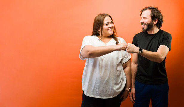 Hispanic couple exchanging a fist bump, celebrating agreement, cooperation, and friendship against an orange background
